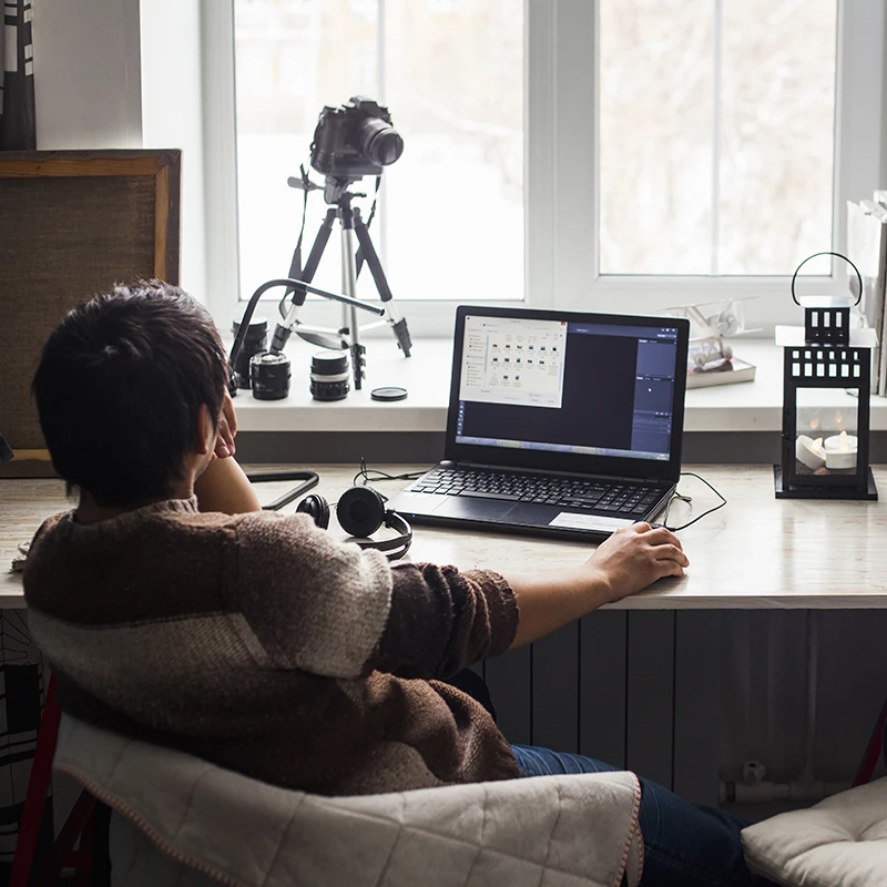 Profesional trabajando desde casa en portátil con monitor externo y cámara en trípode