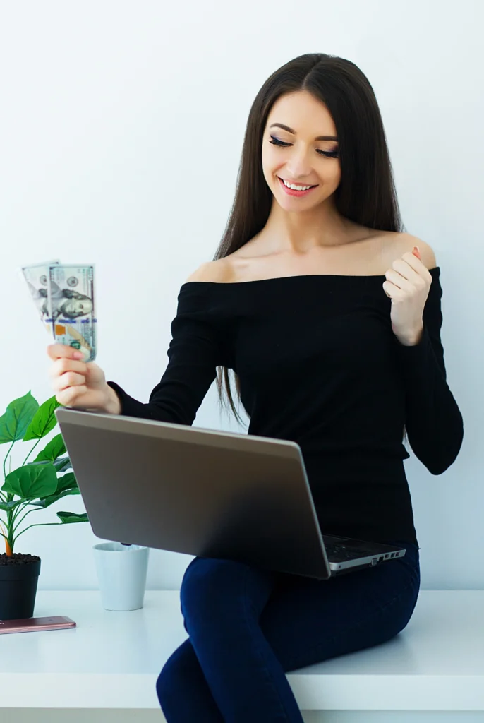 Mujer joven sonriente trabajando con laptop y sosteniendo billetes, representando los ingresos que genera una chatter profesional de OnlyFans desde casa